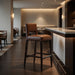 Brown leather bar stool with tall backrest and dark wood frame, tapered legs.