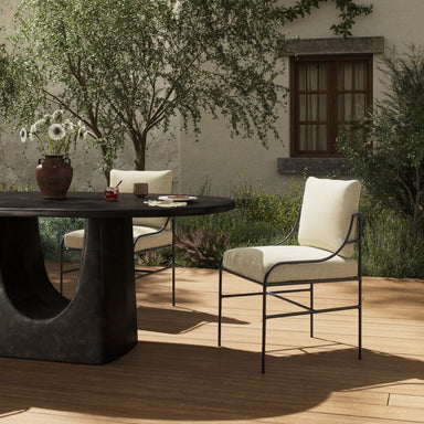 Cream upholstered outdoor dining chair with dark frame on wooden deck, side view.