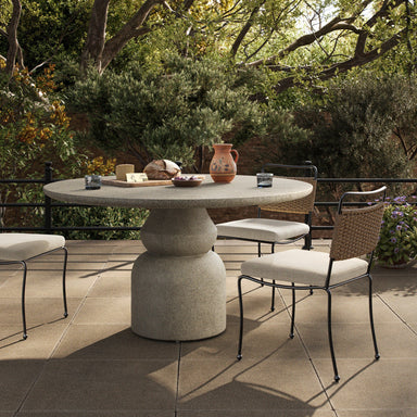 Outdoor round concrete dining table with pedestal base and textured aged natural finish.