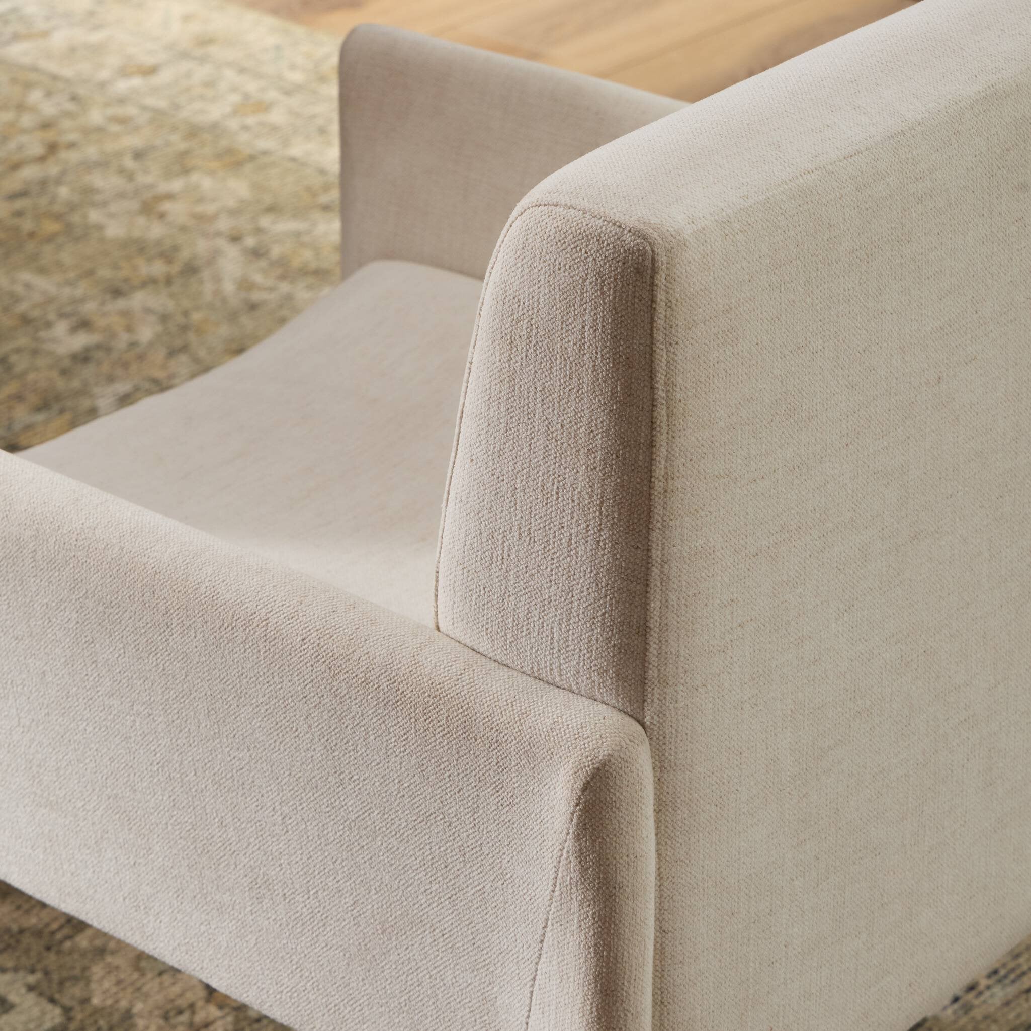 Close-up of off-white upholstered chair arm and seat cushion with stitched seams.