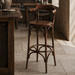 Dark brown wooden bar stool with arched backrest, circular footrest, and curved legs