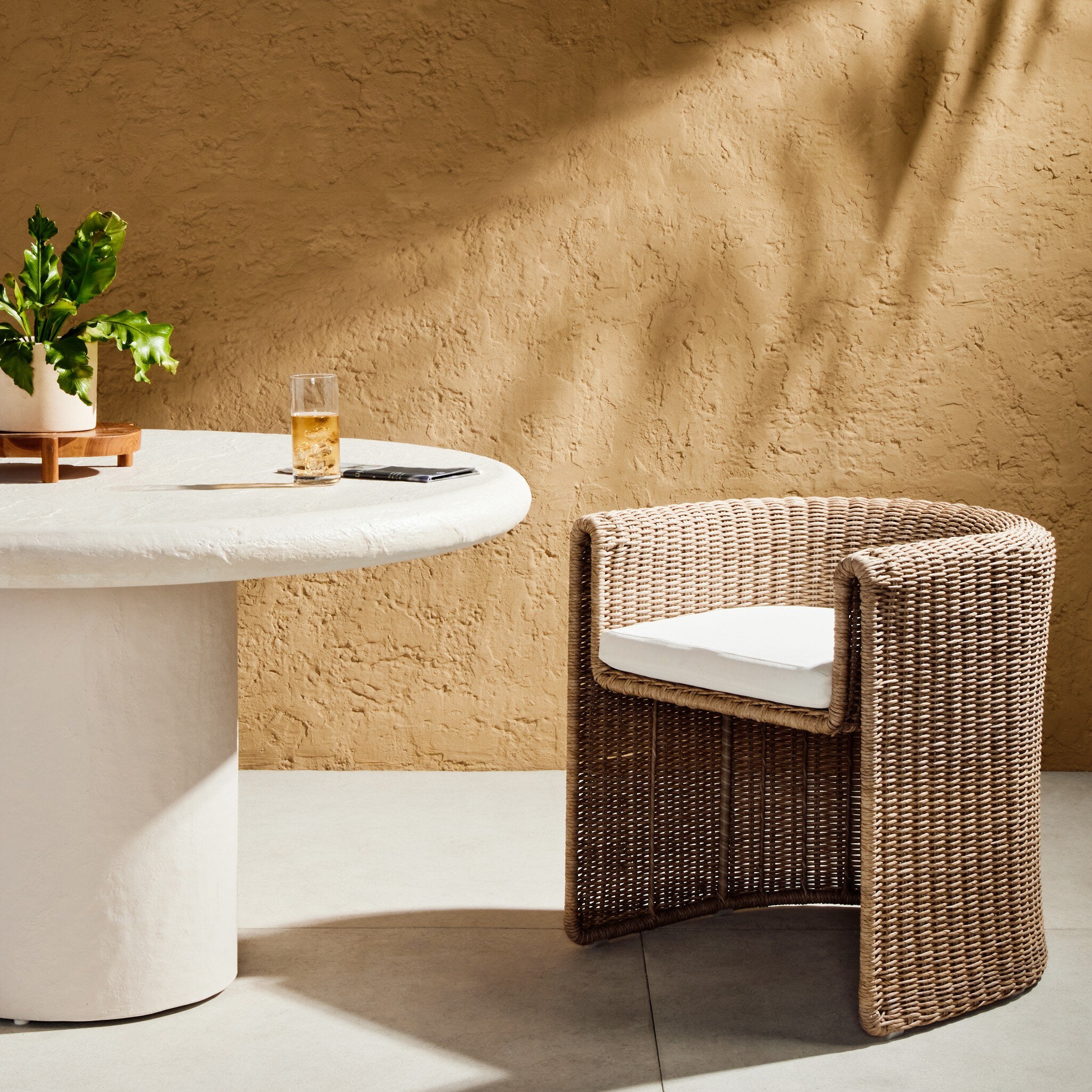 70s-inspired woven outdoor sling chair with waterfall arms and tufted white cushions on yellow background