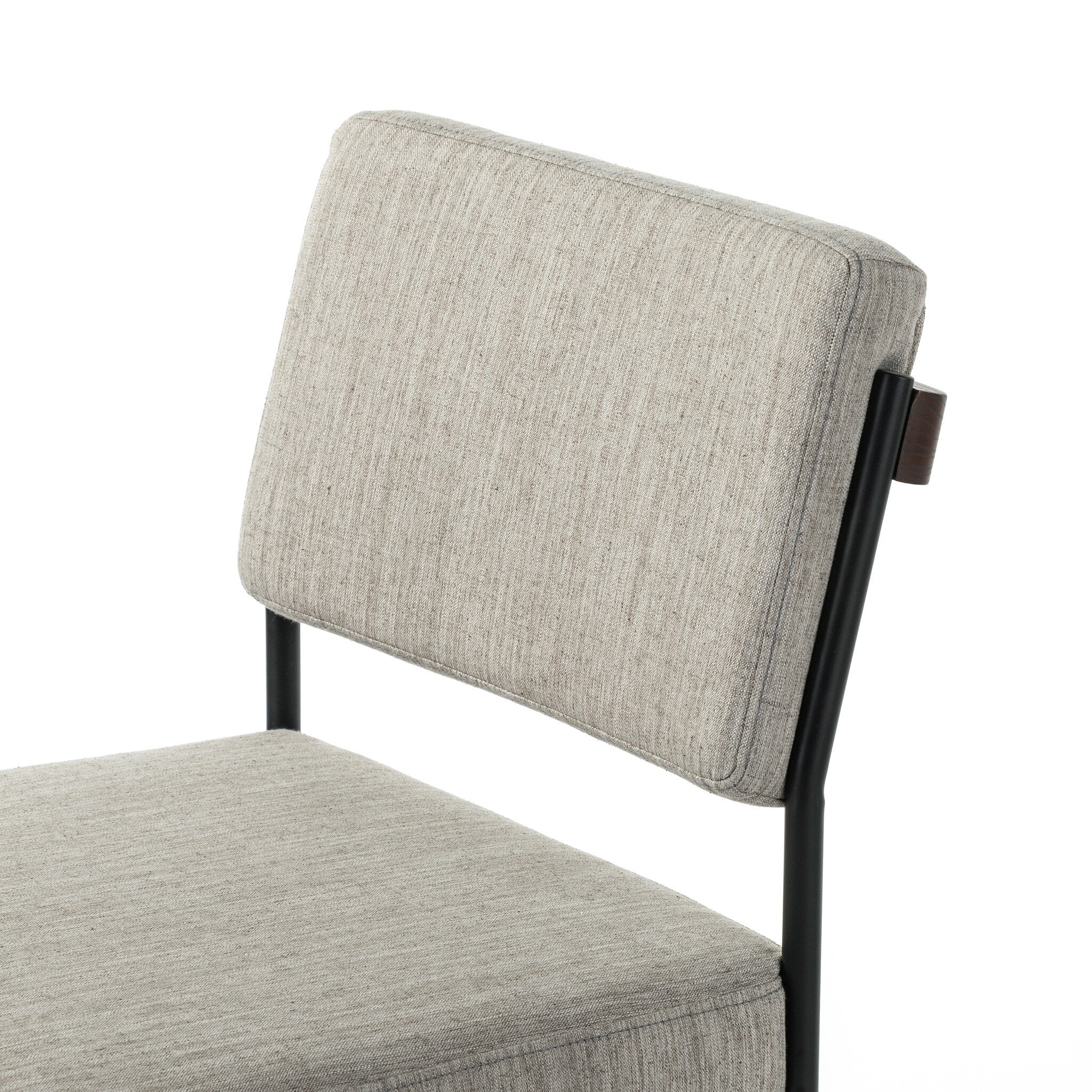 Gray upholstered chair with a black frame on a white background. Angled cushion view Benton Dining Chair in Savile Flannel performance fabric featuring a slim iron frame and wood bar.