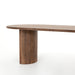 Angled leg view Paden Dining Table in Seasoned Brown Acacia with crescent-shaped legs and an oval tabletop