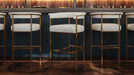 Set of upholstered bar stools with light seats and gold frames in a bar setting.