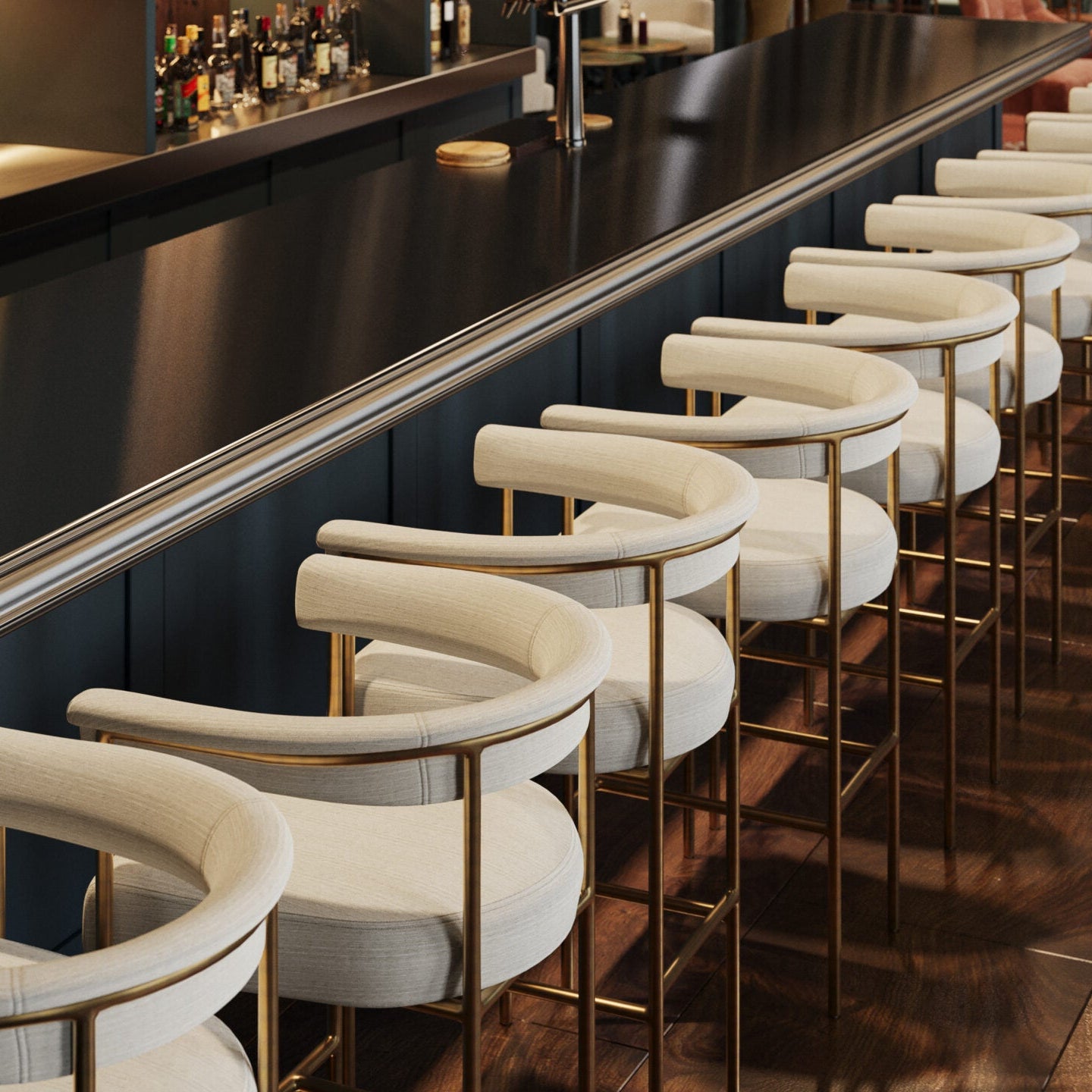 Line of upholstered bar stools with light seats and gold metal frames along a counter.