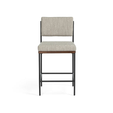 Bar stool with gray cushioned seat and backrest on a white background. Benton Counter Stool in Savile Flannel performance fabric with slim iron frame and nettlewood detailing.