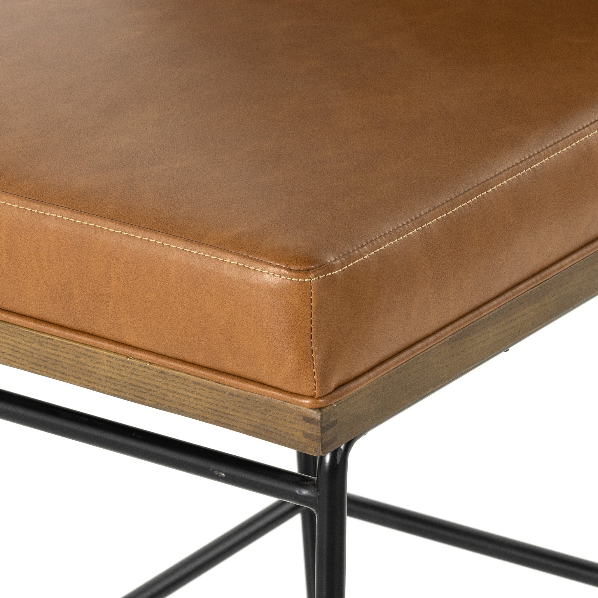 Crete bar stool close-up of tan seat corner with stitched edge and black metal leg