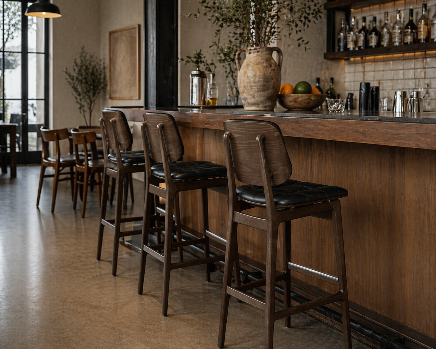 Tufted bar stool with black cushioned seat and back, dark wood frame and footrest