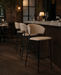 Taupe upholstered bar stool with rounded back, cushioned seat, black metal frame