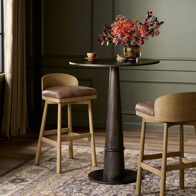 Dining table with two Cloris Swivel Bar Swivel Stool Palermo Cigar Leather Cushion on Solid Oak Wood Base and a vase of flowers in a room with dark walls and a patterned rug.