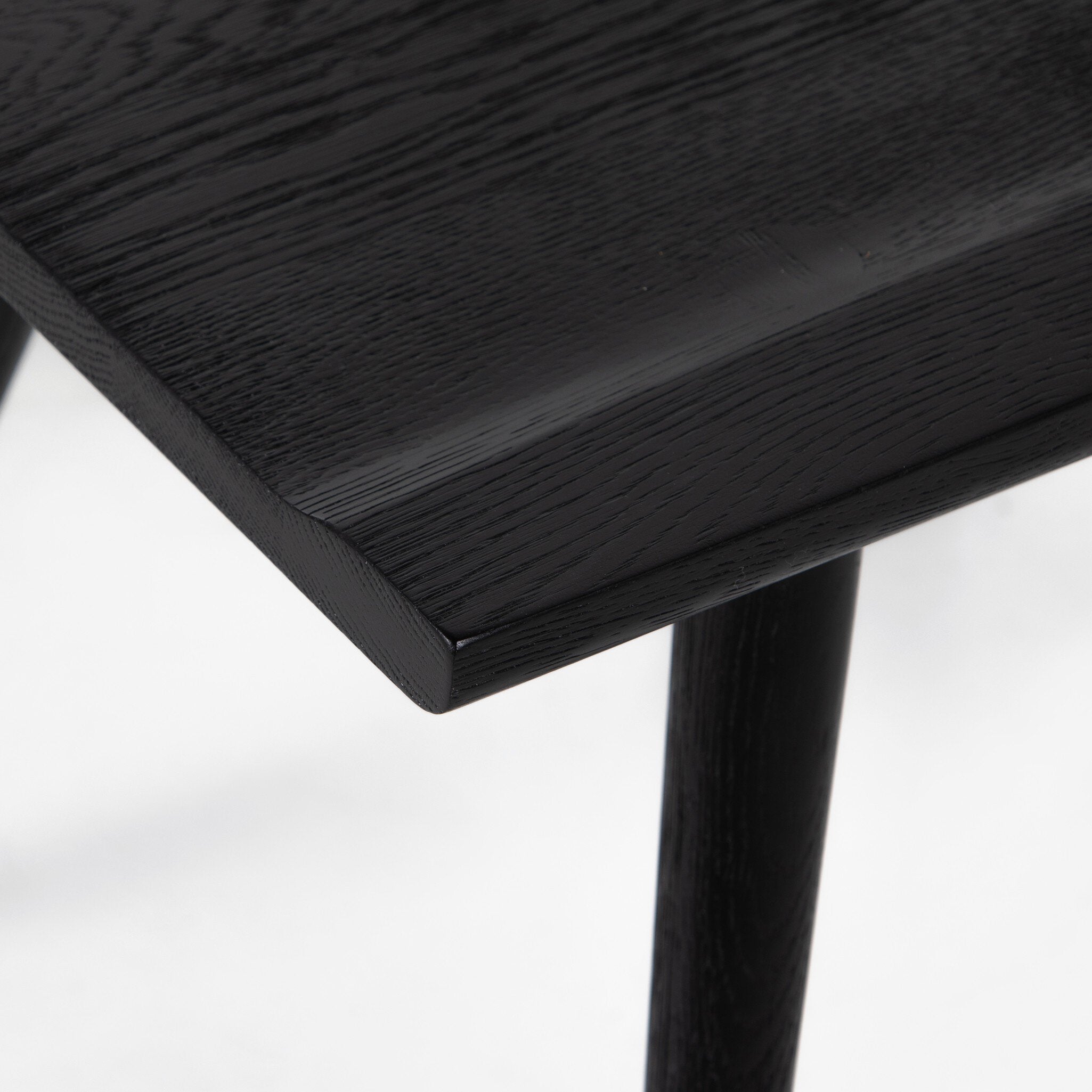 Close-up of a black wooden stool on a white background. Ripley Dining Chair in Black Oak with mid-century Windsor-style sculptural silhouette.