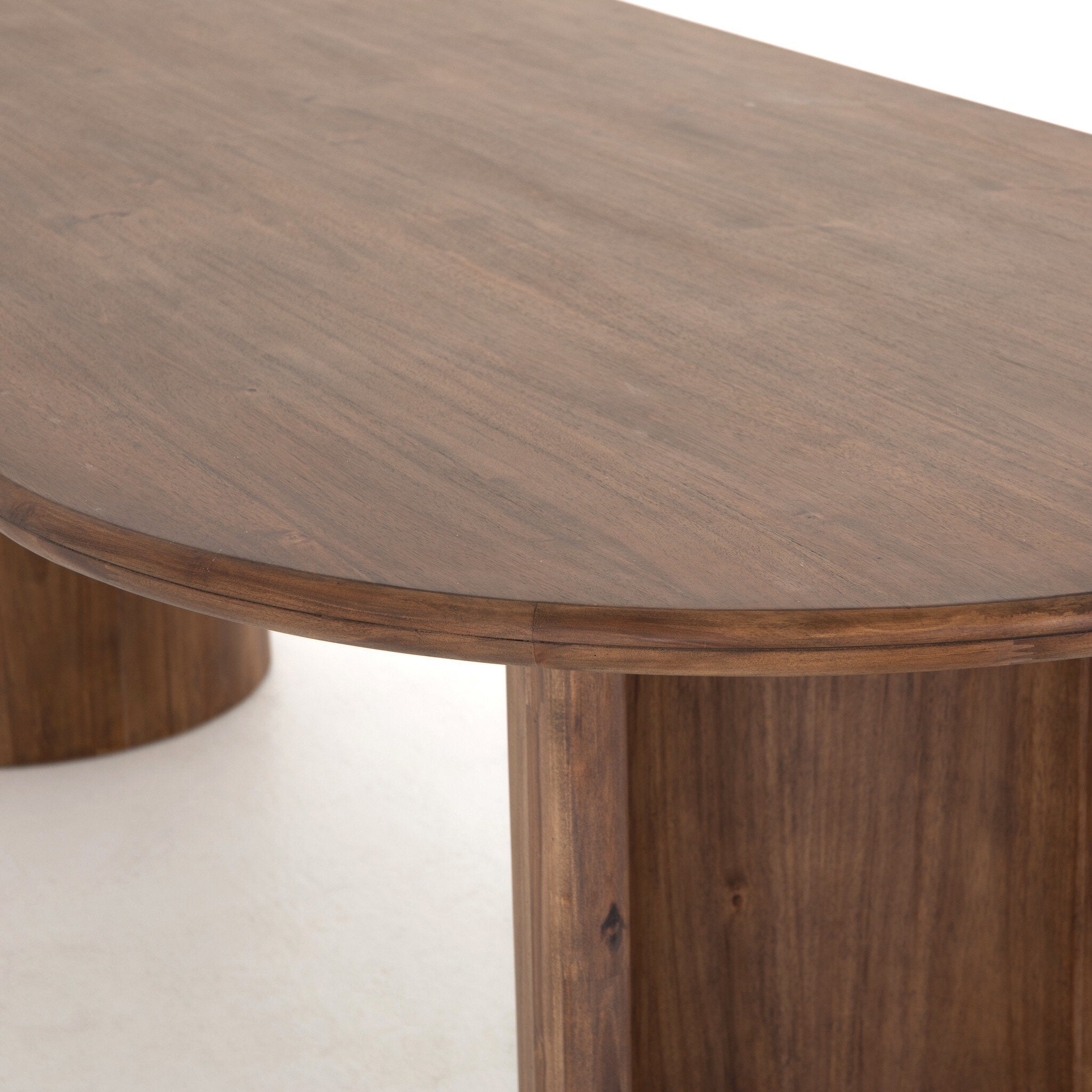 Close wooden detail Paden Dining Table in Seasoned Brown Acacia with crescent-shaped legs and an oval tabletop 