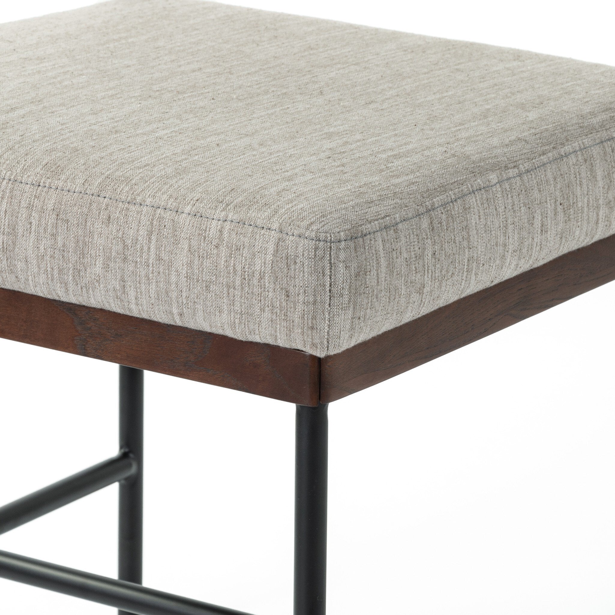 Stool with gray cushioned seat and wooden frame on a white background. Corner chair cushion and wood detail Benton Dining Chair in Savile Flannel performance fabric featuring a slim iron frame and wood bar.