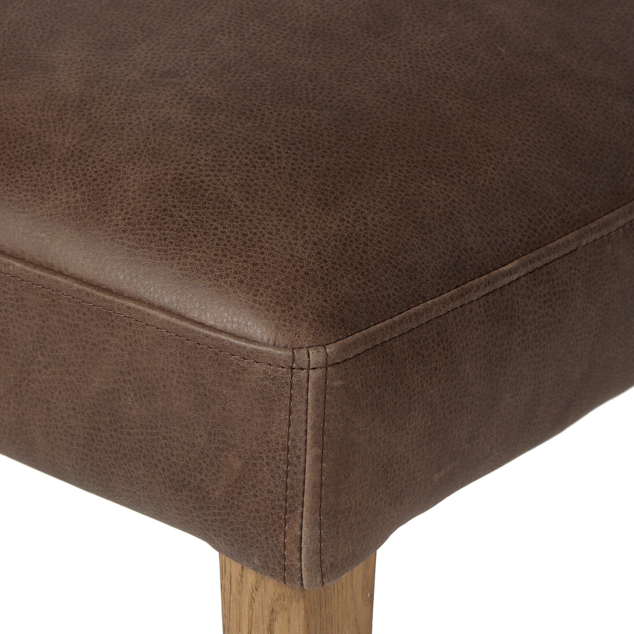 Armless dining chair seat corner with brown upholstered fabric and stitched edges