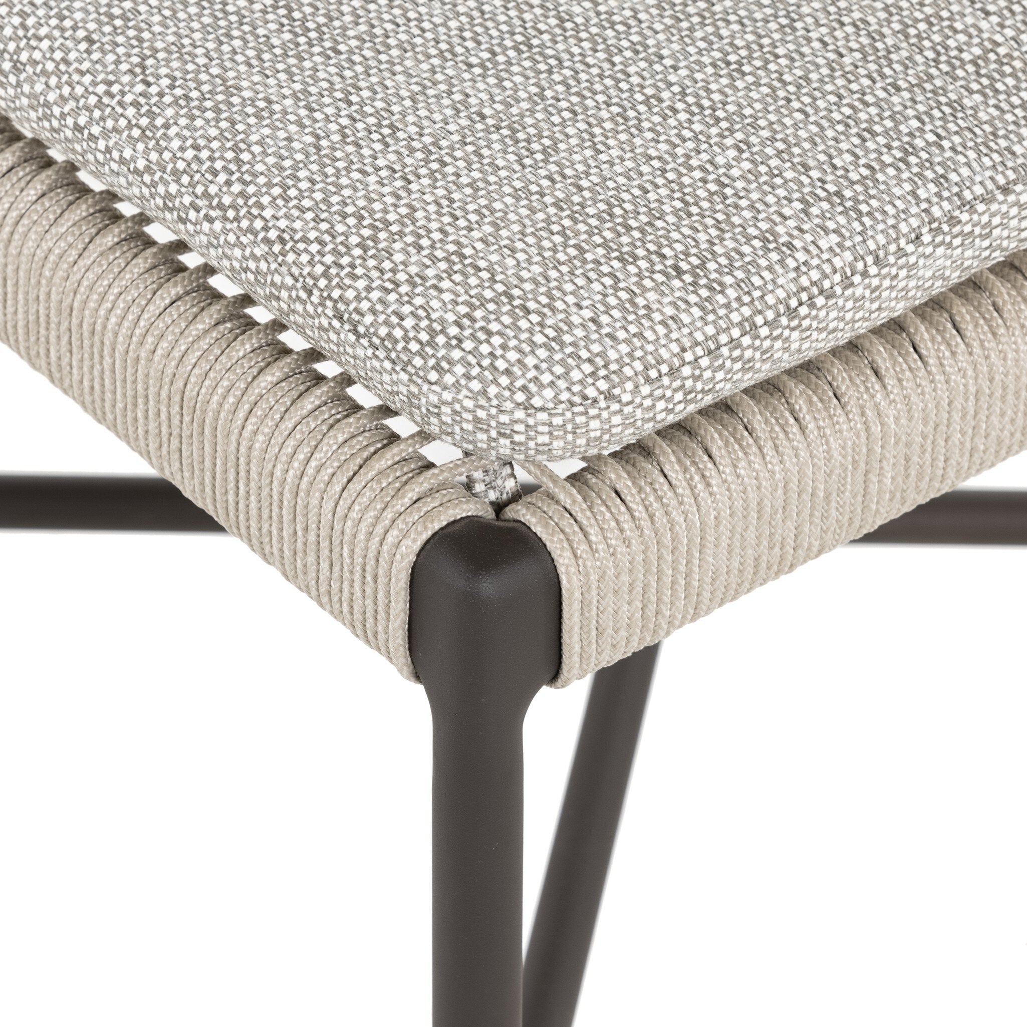 Corner close-up of woven Miller outdoor performance dining chair with a light taupe fabric cushion, wrap detail, and a crossed bronze aluminum frame.