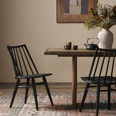 Dining room with wooden table, black chairs, and decorative items on a patterned rug. Lewis Windsor Chair in Black Oak with wire-brushed cathedral grain and tall spindles.