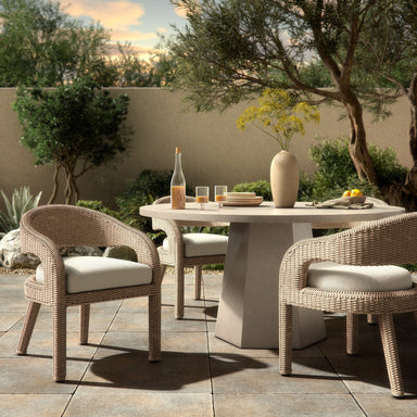 Outdoor patio setting with Hawkins Outdoor Dining Chair in Faye Cream with a barrel-back cutout and woven frame and a round table, featuring a bottle and glasses.