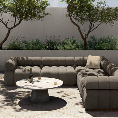 A five-piece sectional sofa with a teak wood base and upholstered in a brown fabric, featuring a modular design with a small round table in an outdoor setting with trees and plants.