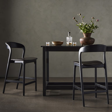 Dining scene Amare Counter Stool with monochromatic top-grain black leather seat and minimalist black-finished Scandinavian solid ash wood base