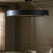 Black pendant light fixture Baum Chandelier with a rounded dark-finished frame and bronzed stainless steel suspension hanging in a room with panelled walls and a vase on a table.