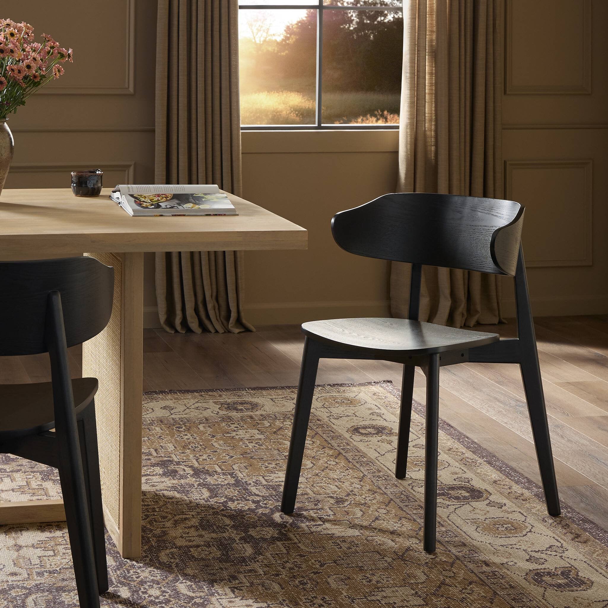 Black armless dining chair with curved backrest and round seat beside table
