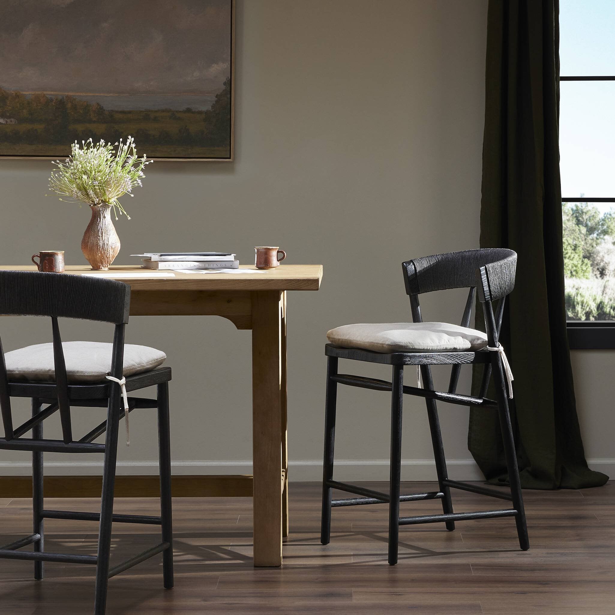 Bar stool with black frame, rounded upholstered back, and cream seat cushion