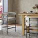 Upholstered counter stool in light camel fabric with armrests and black metal frame