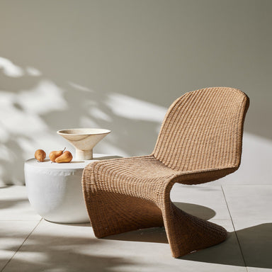Portia Outdoor Occasional Chair with solid teak frame and grey rope-weave seating next to a white table with a bowl and fruits on a light wooden floor.