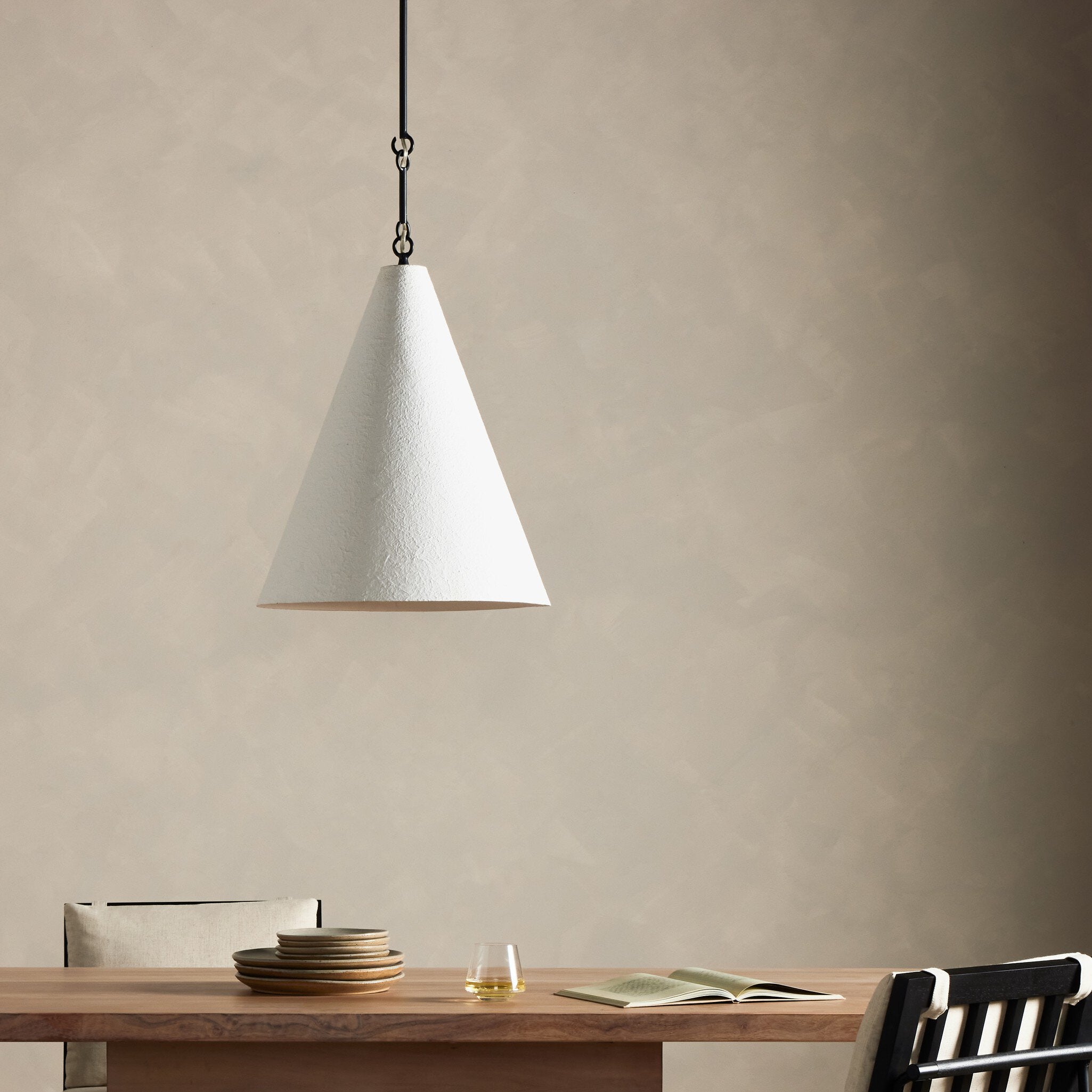 Conical pendant light Grazia matte white plaster with antiqued iron hardware hanging above a wooden table with minimal decor against a beige wall