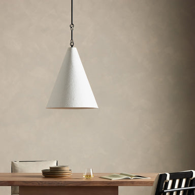 Conical pendant light Grazia matte white plaster with antiqued iron hardware hanging above a wooden table with minimal decor against a beige wall