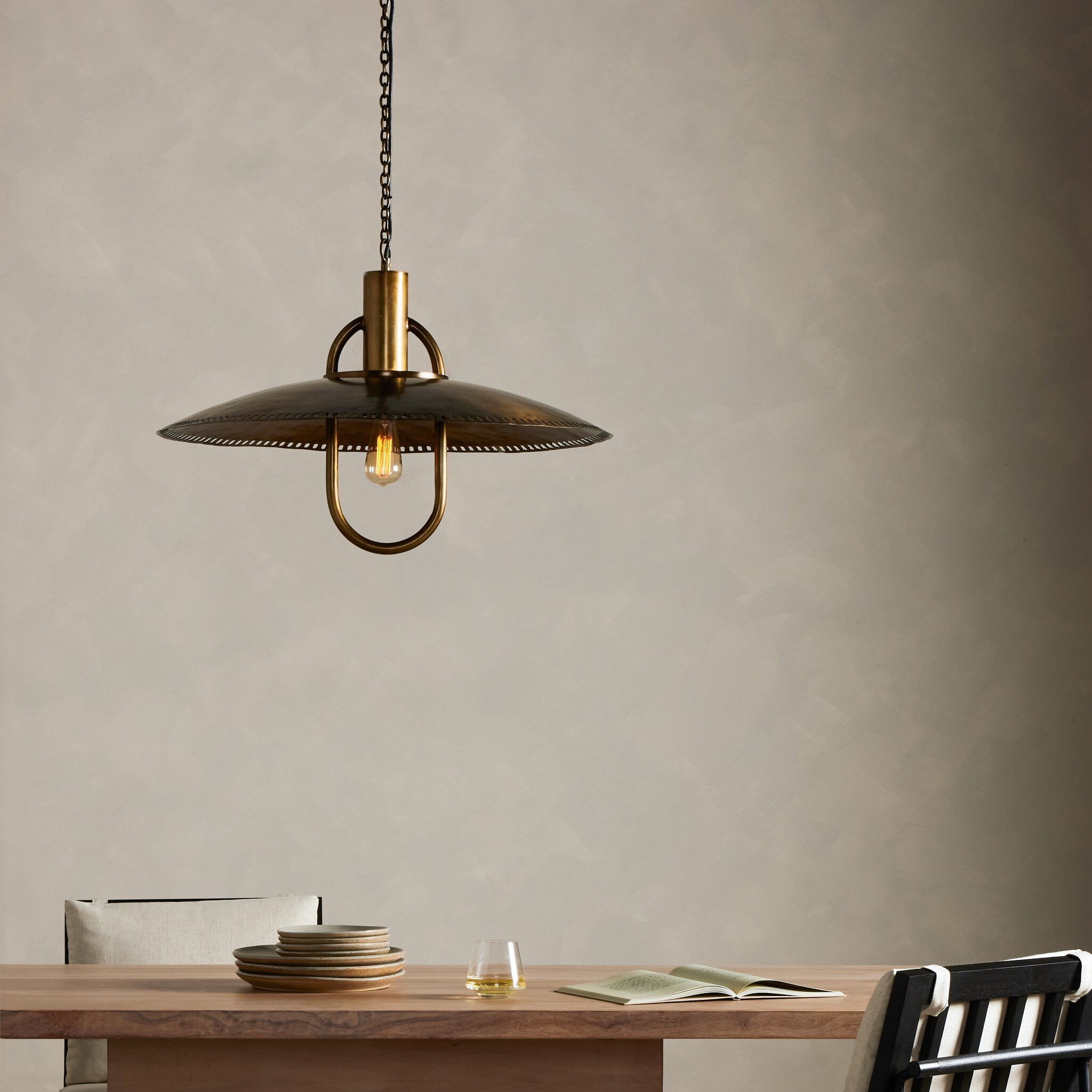 Arely 30-inch industrial pendant light in dark antique brass with perforated dome above dining table setting showcasing mid century modern vintage inspiration