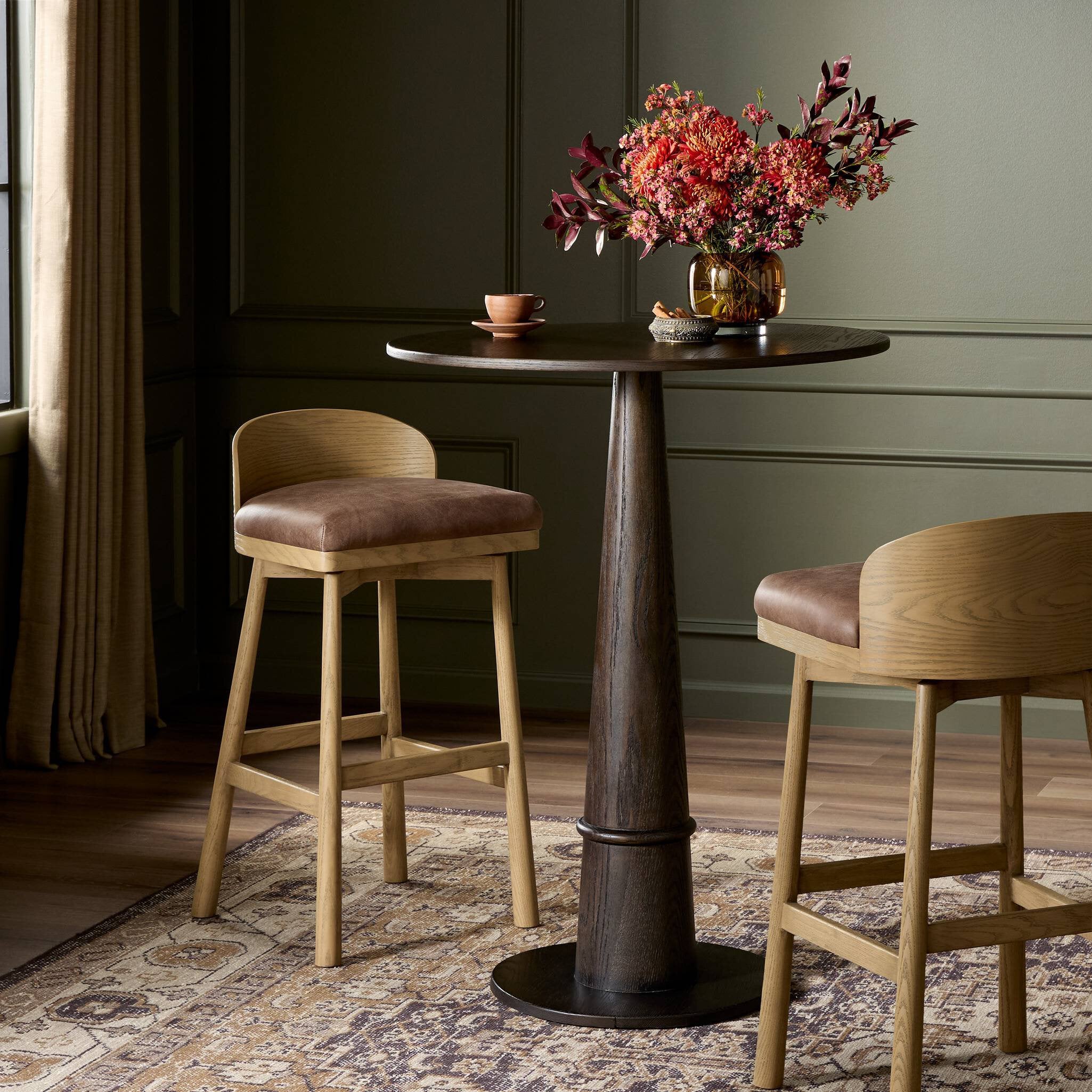 Dining table with two Cloris Swivel Bar Stool and a vase of flowers in a room with dark walls and a patterned rug.