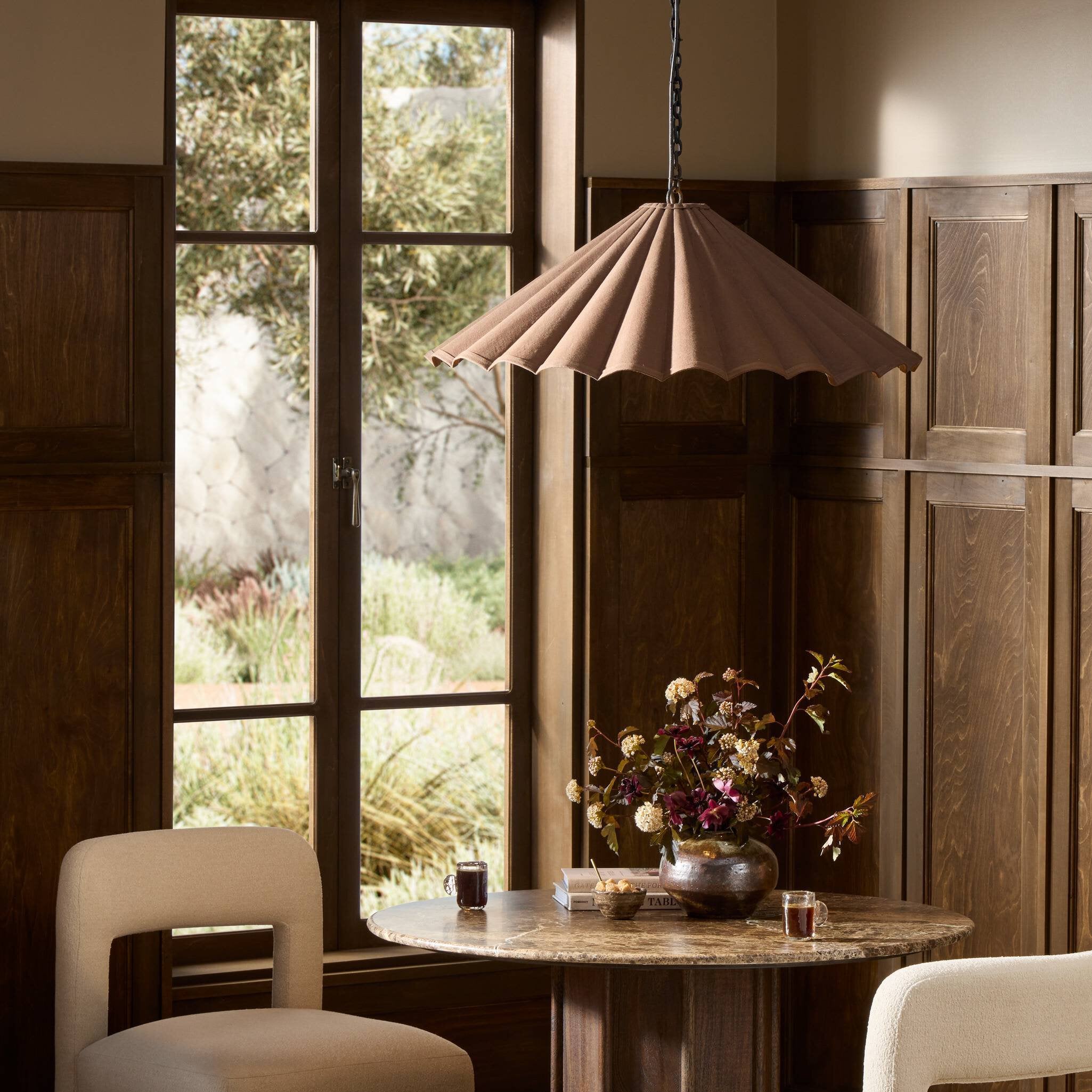 Cozy modern wooden venue showing Fiorella 34-inch scalloped espresso brown canvas pendant light with antiqued brass interior over a large dining table scene.