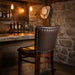 Fudge Brown Restaurant Court Drake Wood Bar Stool with a rectangular upholstered backrest, padded seat, and a dark wood frame with a footrest