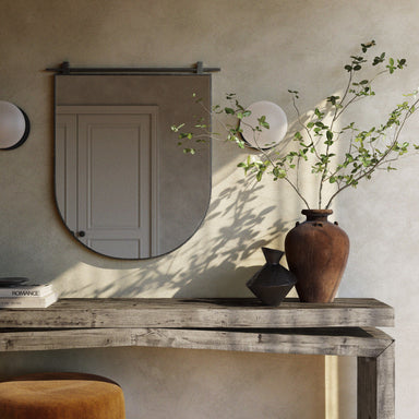 Decorative setup with a wooden console table, Chico small arch wall mirror with a vertical antiqued iron suspension bar, and vase against a neutral wall