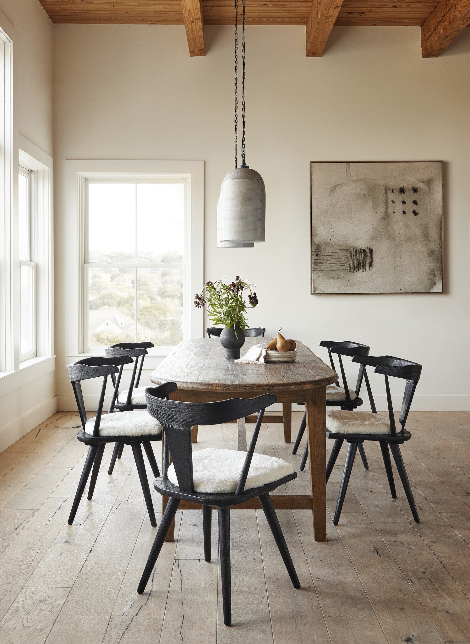 Dining room with wooden table and black chairs, pendant light, and abstract painting. Hospitality view Ripley Dining Chair in Black Oak with mid-century Windsor-style sculptural silhouette.