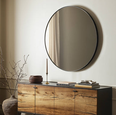 Bellvue round mirror with a classic black iron frame hanging on a wall above a wooden cabinet with decorative items