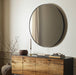 Bellvue round mirror with a classic black iron frame hanging on a wall above a wooden cabinet with decorative items