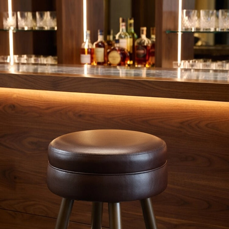 Brown round padded bar stool seat with chrome footrest and tapered legs