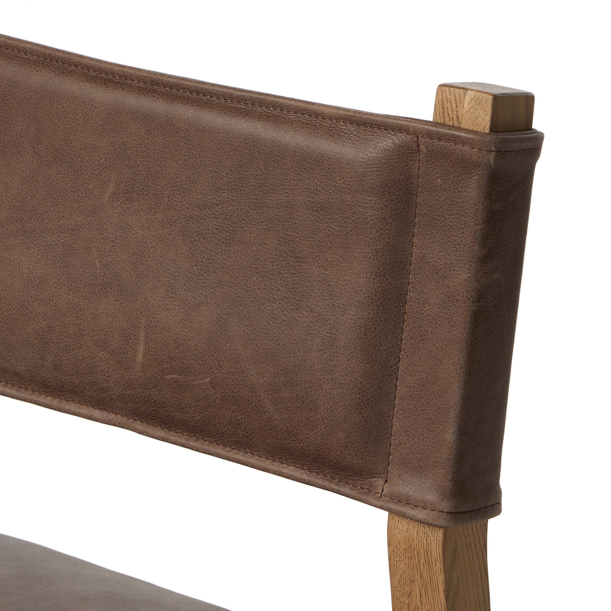 Brown upholstered chair back close-up with top corner and wood support post.
