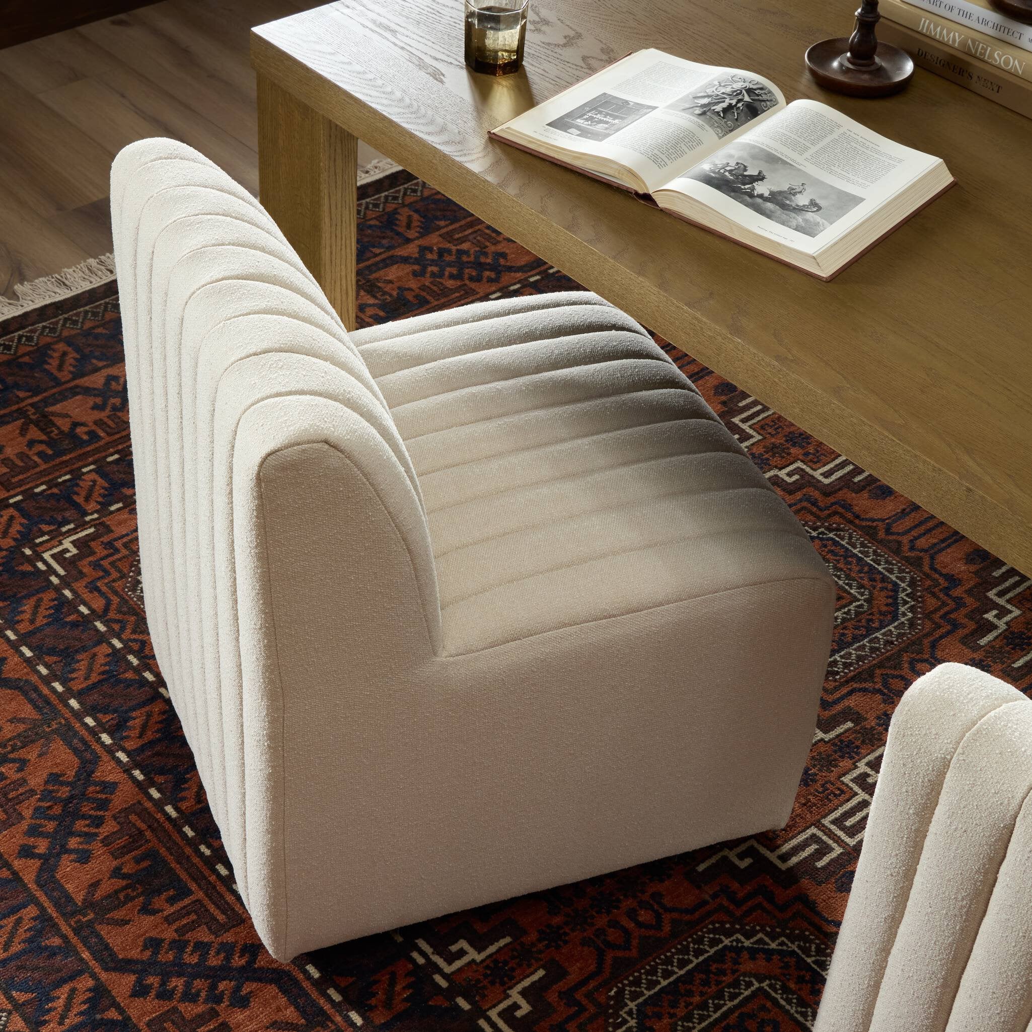 Beige armchair on a patterned rug with an open book on a wooden table.
