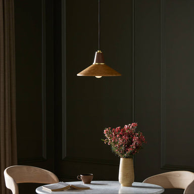 Modern interior with a mid century Cullen pendant light with a camel leather shade and natural walnut finial, table, chairs, and a vase with flowers against a dark wall
