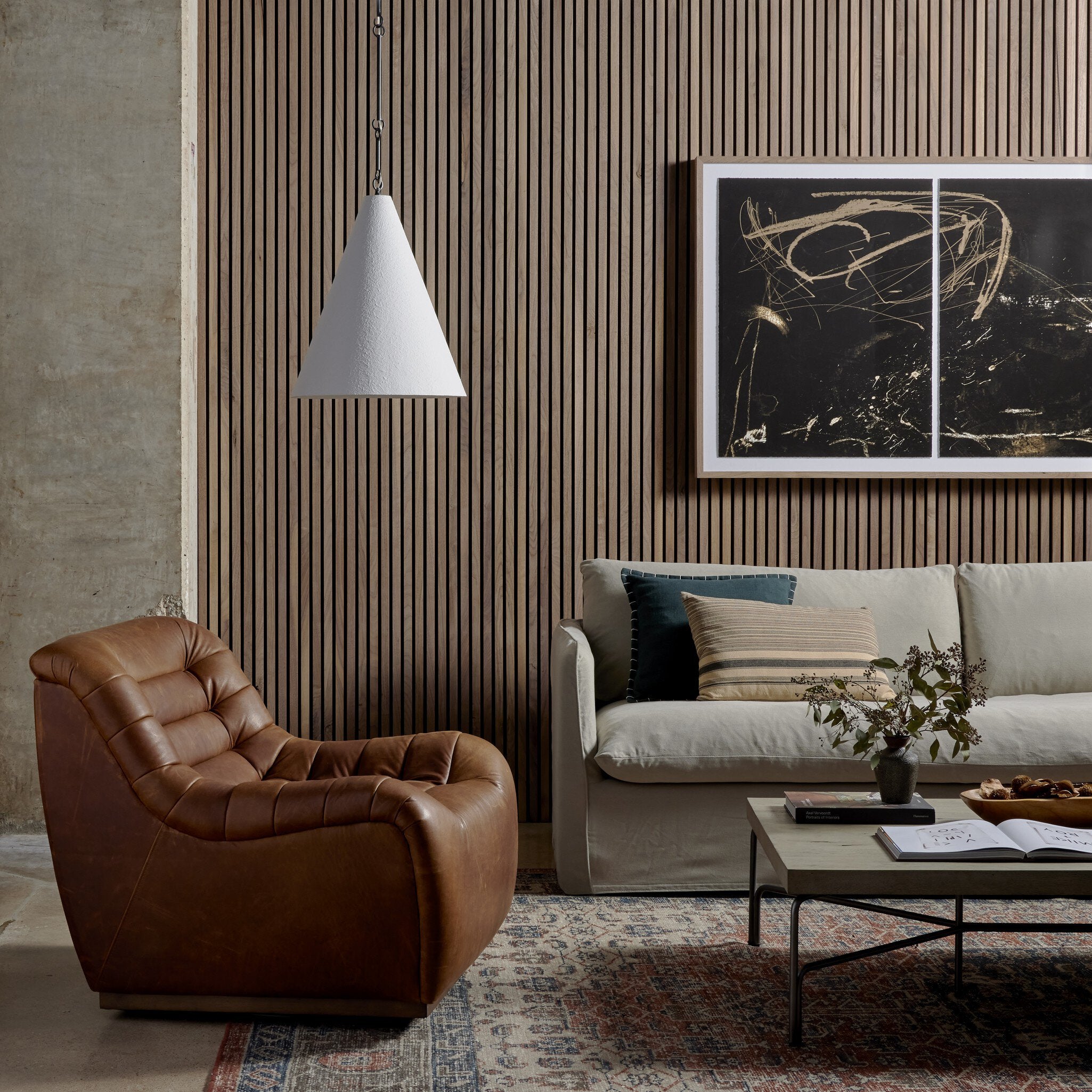Grazia matte white plaster pendant light with antiqued iron hardware showing Modern living room with brown leather armchair, beige sofa, and abstract art on the wall.