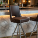 Porcini Fudge Brown Sterling Bar Stool with a curved upholstered backrest, padded seat, and a sleek chrome frame with a footrest in hospitality