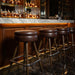 Set of brown bar stools with round padded seats, chrome footrests, turned legs