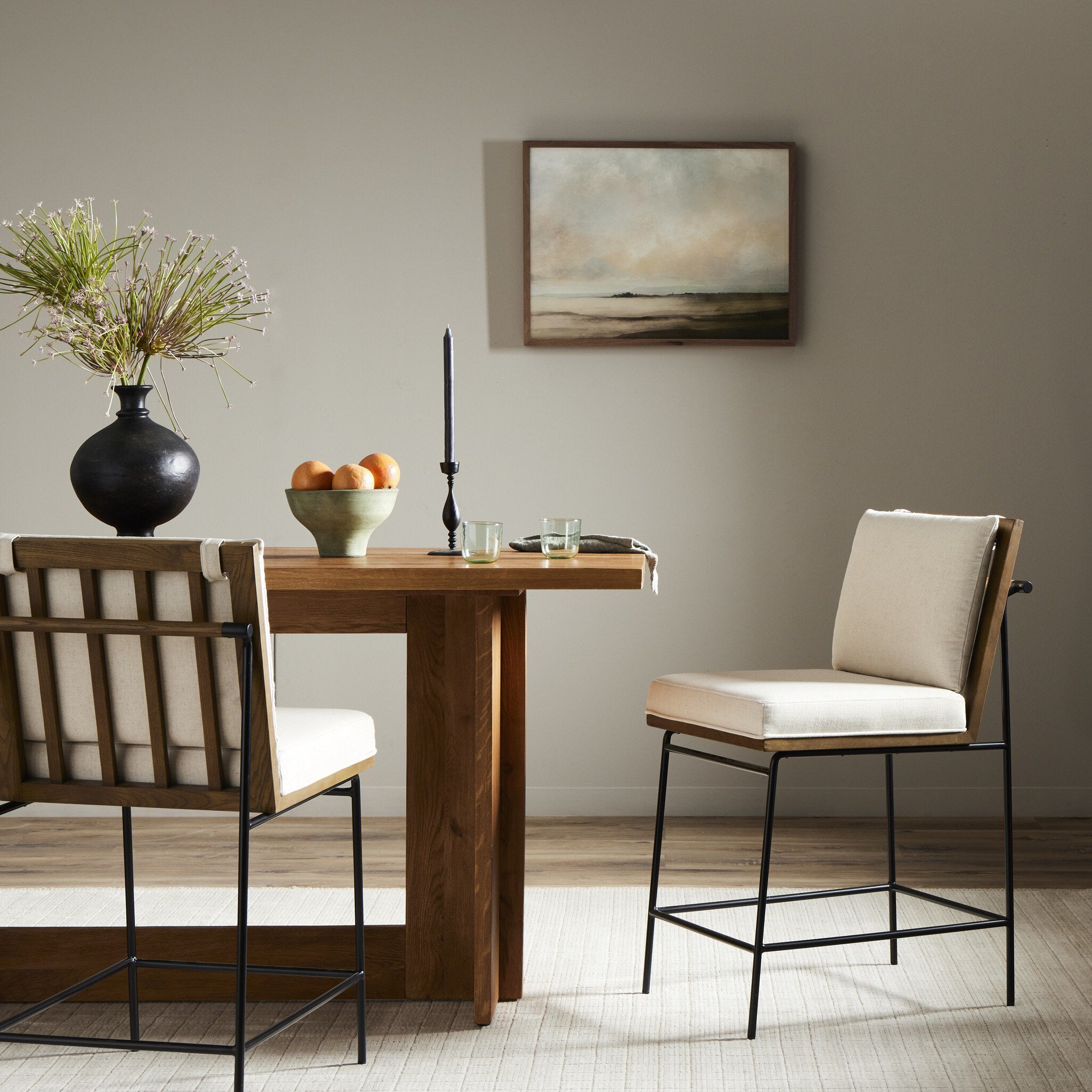 Counter stool with beige fabric seat and backrest on black metal frame, in dining setting