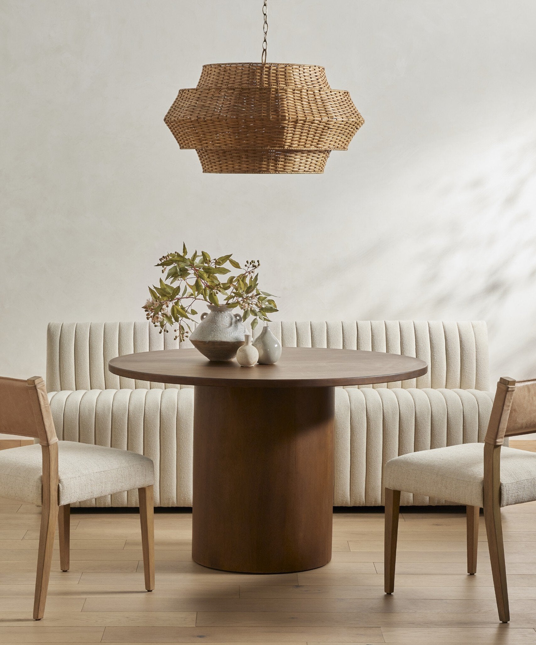 Dining room with a round wooden table, chairs, and a wicker pendant light.