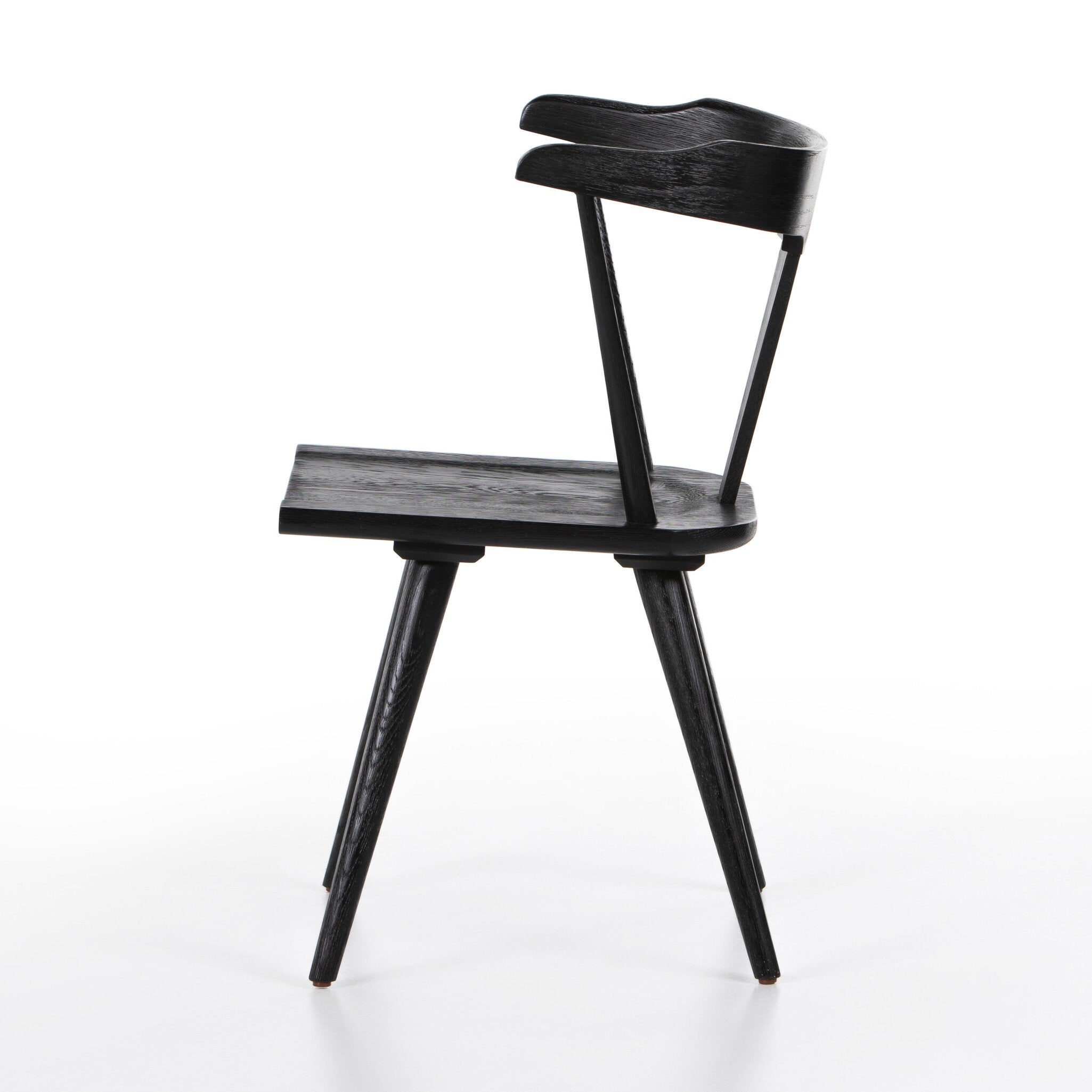 Black wooden chair on a white background. Side view Ripley Dining Chair in Black Oak with mid-century Windsor-style sculptural silhouette.
