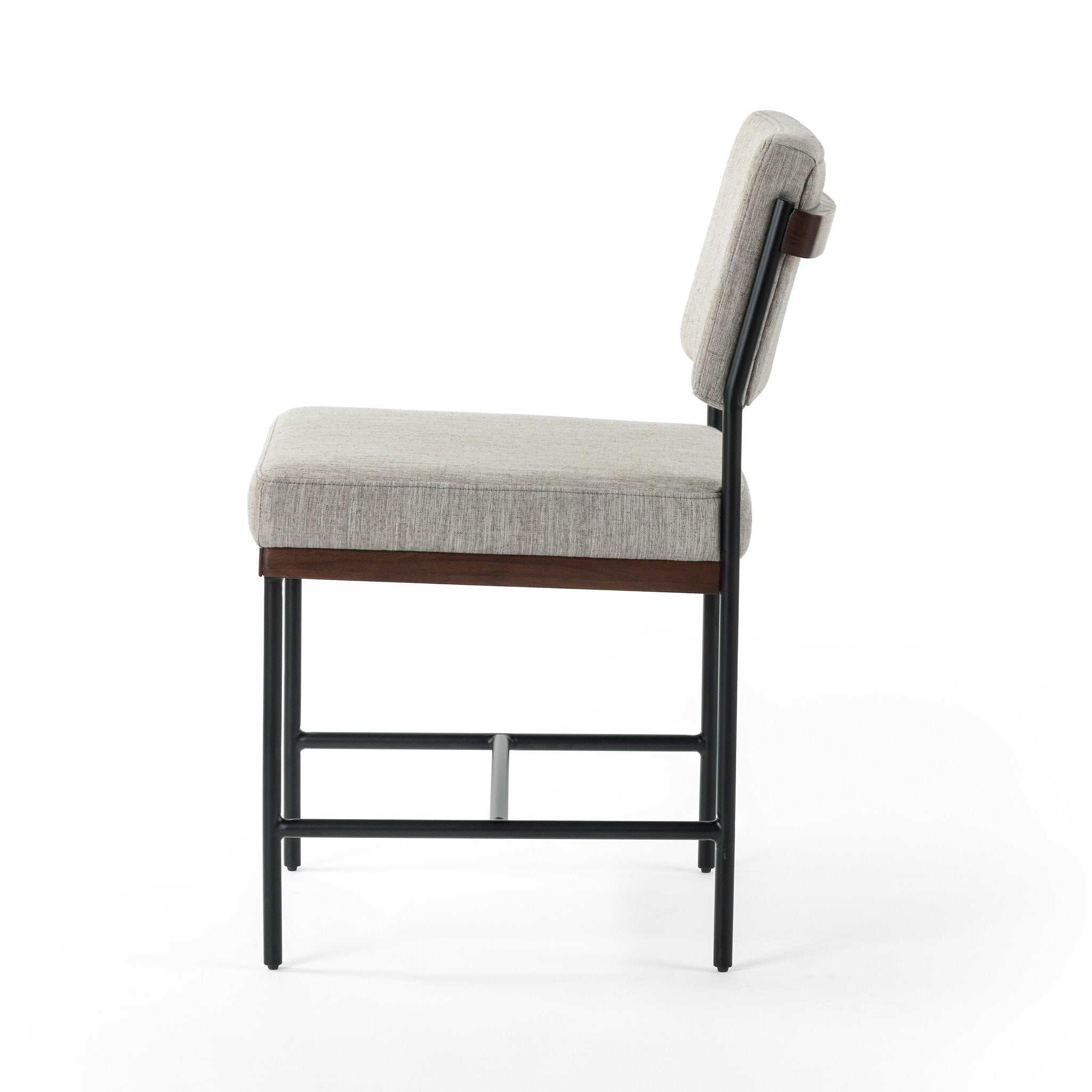 Gray cushioned chair with wooden legs on a white background. Side view Benton Dining Chair in Savile Flannel performance fabric featuring a slim iron frame and wood bar.